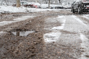 Road with pits and puddles. Parked cars covered with snow