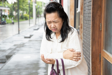 old asian senior woman suffers from elbow joint pain or arm bone osteoporosis; concept of tennis...