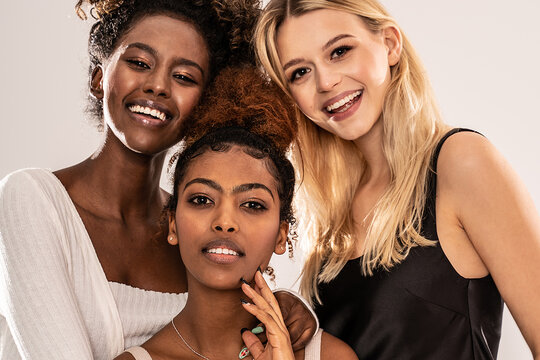 Three attractive young multiethnic women looking at camera, smiling.