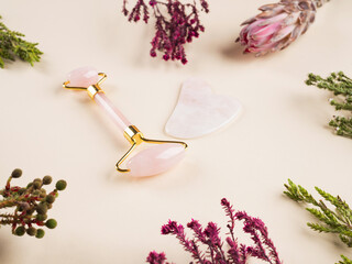Pink quartz guasha face roller on floral background. Chinese beauty massage tool.