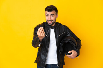 Caucasian man with a motorcycle helmet over isolated yellow background making money gesture
