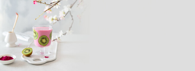 Pink matcha smoothie banner. Matcha smoothie with banana and kiwi in a glass on light background with sakura branches. Copy space.