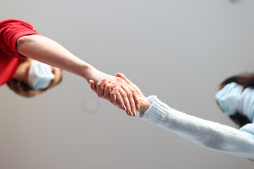 Two women in protective medical masks shake hands