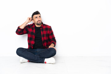 Young handsome man sitting on the floor having doubts and with confuse face expression