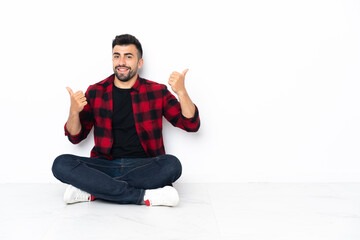 Young handsome man sitting on the floor with thumbs up gesture and smiling