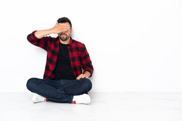 Young handsome man sitting on the floor covering eyes by hands. Do not want to see something