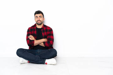Young handsome man sitting on the floor with arms crossed and happy