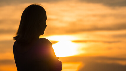 Silhouette of a young pensive woman at sunset looking into the distance