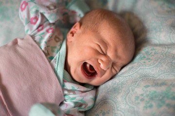 A newborn Baby in pink and turquoise clothes is crying. Close up