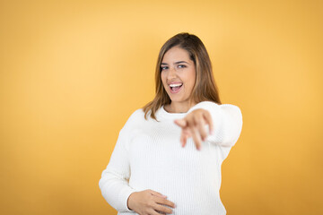 Young caucasian woman over isolated yellow background laughing at you, pointing finger to the camera with hand over body, shame expression