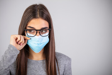 Woman wiping foggy glasses caused by wearing medical mask indoors, closeup. Woman wiping foggy glasses caused by wearing disposable mask on gray background, closeup.