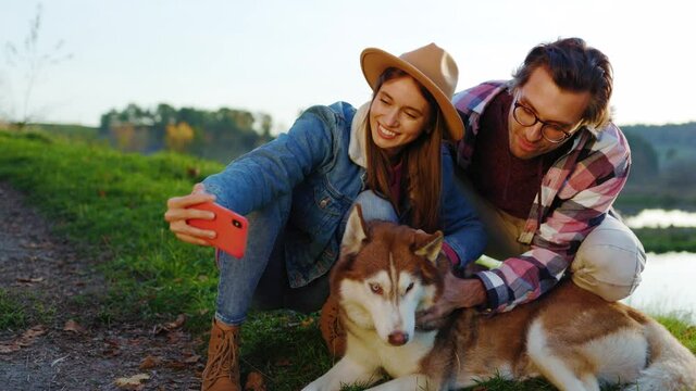 Lovely couple with a dog taking selfie photo on phone in autumn forest near lake. Landscape vacation relationship pets. Outdoors nature. Slow motion