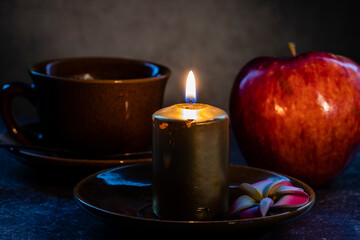 A wax candle with a Cup of coffee and an Apple is burning.