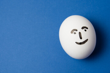 Egg with a happy face on a blue background with copy space.