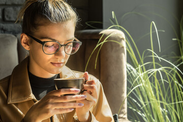 Young woman drinking coffee cup and sitting in cafe. Girl in glasses pauses after work.