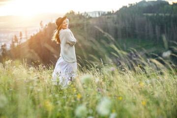 Fototapeta na wymiar Happy woman enjoying sunset stay on the green grass on the forest peak of mountain. Fresh air, Travel, Summer, Health care, authenticity, sense of balance and calmness 