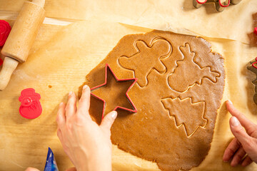 Young woman cutting gingerbread dough in to different shapes on brown baking paper. Getting ready for christmas.
