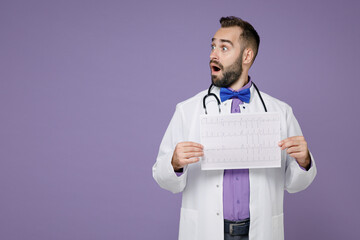 Shocked doctor man in medical gown stethoscope hold electrocardiogram record, heart ekg cardiogram chart of wave in paper isolated on violet background. Healthcare personnel health medicine concept.