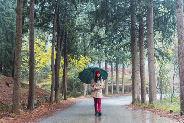 mujer chica con paraguas entre pinos arboles lloviendo en la sierra monte feliz sonriendo