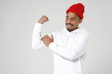 Strong puzzled young african american man 20s years old wearing basic casual streetwear hoodie standing showing biceps muscles looking camera isolated on white colour wall background studio portrait.