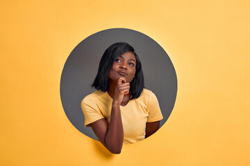 Portrait of a thoughtful young  woman looking up in a round hole circle in orange background. Copy...