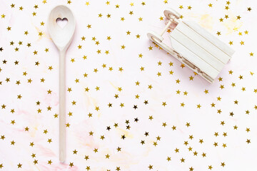 Stirring spoon, sleigh and golden stars decoration on a pink background. Winter holidays cooking festive dinner, Christmas and New Year menu and celebration concept. Top view, flat lay, copy space