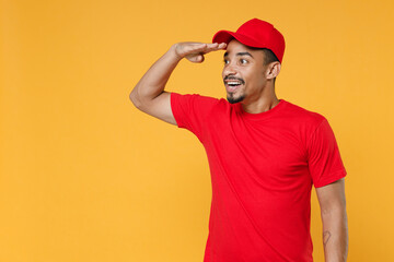 Delivery employee african man 20s in red cap blank print t-shirt uniform workwear work courier dealer service during quarantine coronavirus covid-19 virus concept isolated on yellow background studio.