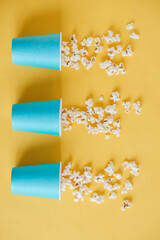 Popcorn in blue paper cups scattered on a yellow background. Top view. Copy, empty space for text