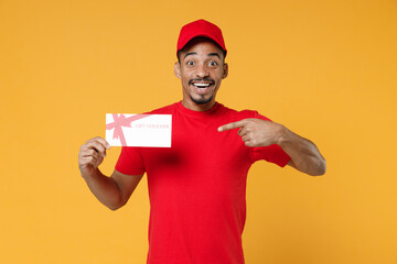 Delivery employee african man 20s in red cap blank print t-shirt uniform workwear work courier dealer service concept hold mockup gift certificate voucher coupon isolated on yellow background studio.
