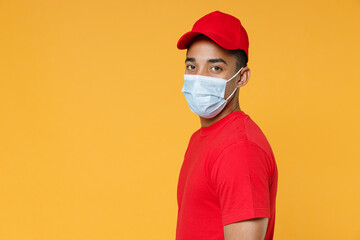 Fototapeta na wymiar Side view delivery employee african man in red cap blank print tshirt face mask gloves work courier dealer service on quarantine coronavirus covid19 virus concept isolated on yellow background studio