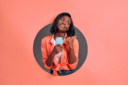 Young afro american woman texting using smartphone over isolated background pointing and showing with thumb up to the side with happy face smiling. Copy space.
