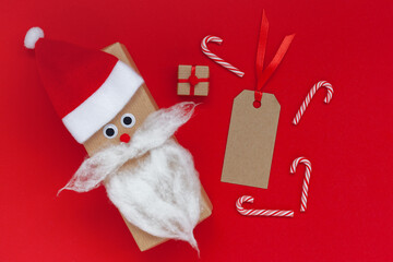 Creative christmas gift box in the form of Santa hat and beard with empty tag and present on red background.
