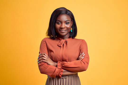 Advertising concept. Confident and smiling young african american woman crossed hands on chest, looking at camera and standing on yellow copy space background.