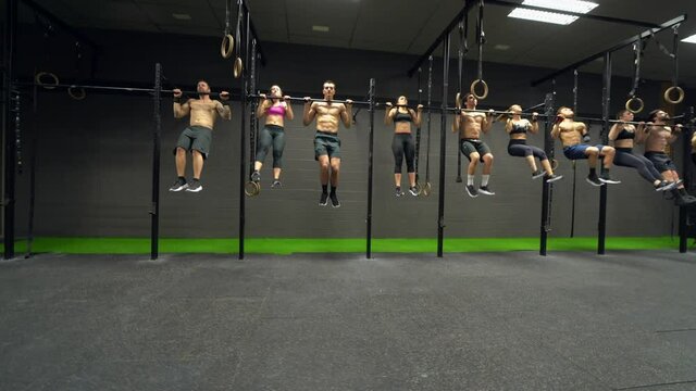 Group of athletes exercising chin-ups on rod at gym
