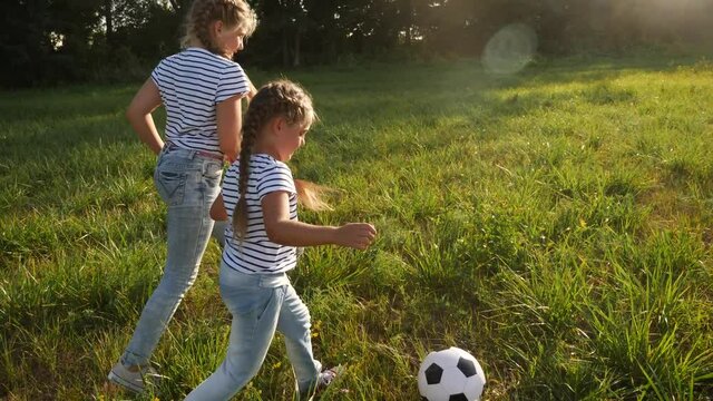 two little girls play soccer in the park with a ball. kid dream concept. kid play ball on green grass in the park. child playing soccer. people fun in the park concept