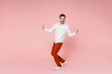 Full length side view of happy joyful young bearded man 20s wearing basic casual white shirt standing doing winner gesture looking camera isolated on pastel pink color wall background studio portrait.