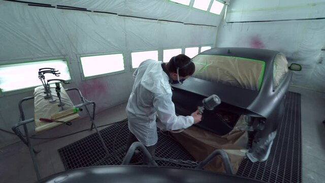 Car body painter spraying car boot in paint booth