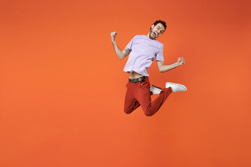 Fototapeta na wymiar Full length of overjoyed screaming young bearded man 20s wearing casual violet t-shirt jumping doing winner gesture clenching fists looking camera isolated on bright orange background studio portrait.