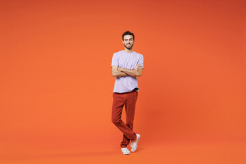 Fototapeta na wymiar Full length of smiling handsome attractive young bearded man 20s wearing casual basic violet t-shirt standing holding hands crossed looking camera isolated on bright orange background studio portrait.
