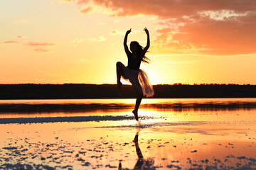 Fototapeta premium Tender girl young ballerina in pink transparent in a graceful jump on the lake at sunset.