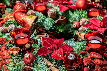 Traditional romantic Christmas table decoration. Christmas wreath with red poinsettias, balls and red candles between fir branches, selective focus. 