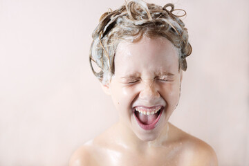 a little blonde girl in the bathroom with foam on her head laughs happily with her mouth open