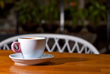 White coffee cup on a wooden board. Blurred bar interior on background. Free space near the coffee.
