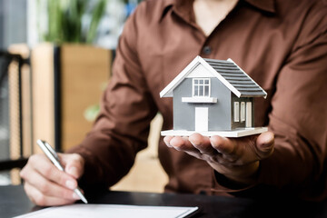 Close-up of a man holding a small house. Concept of purchasing new apartment.