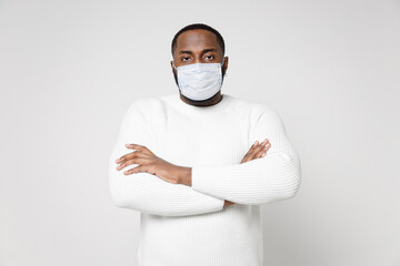 Displeased young african american man in basic sweater sterile face mask safe from coronavirus virus covid-19 during quarantine holding hands crossed isolated on white wall background studio portrait.