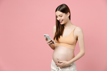 Young pregnant woman future mom in basic top belly stomach tummy hold mobile cell phone using app for baby isolated on pastel pink background studio Maternity family pregnancy expectation concept