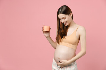 Pregnant woman future mom in top with belly stomach tummy with baby hold applying cream for stretch marks striae isolated on pink background studio Maternity family pregnancy expectation concept