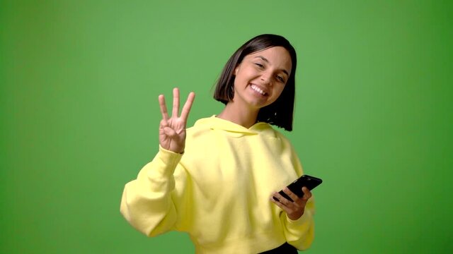 Young woman using mobile phone on green screen chroma key background happy and counting with fingers