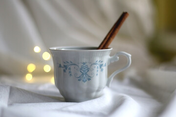Vintage porcelain cup with warm beverage and cinnamon stick. Selective focus, bokeh lights.
