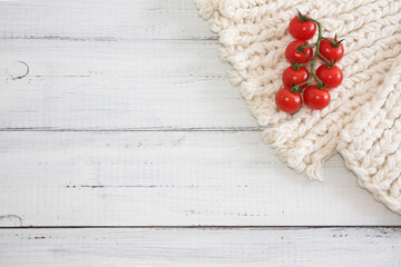 Red tomatoes cherry on white soft surface, wooden table background. Copy space. Selective focus.